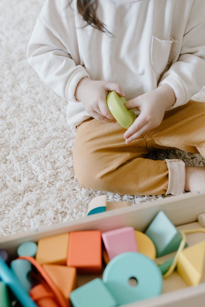 Young child sitting on a carpet playing with colorful educational toys indoors.