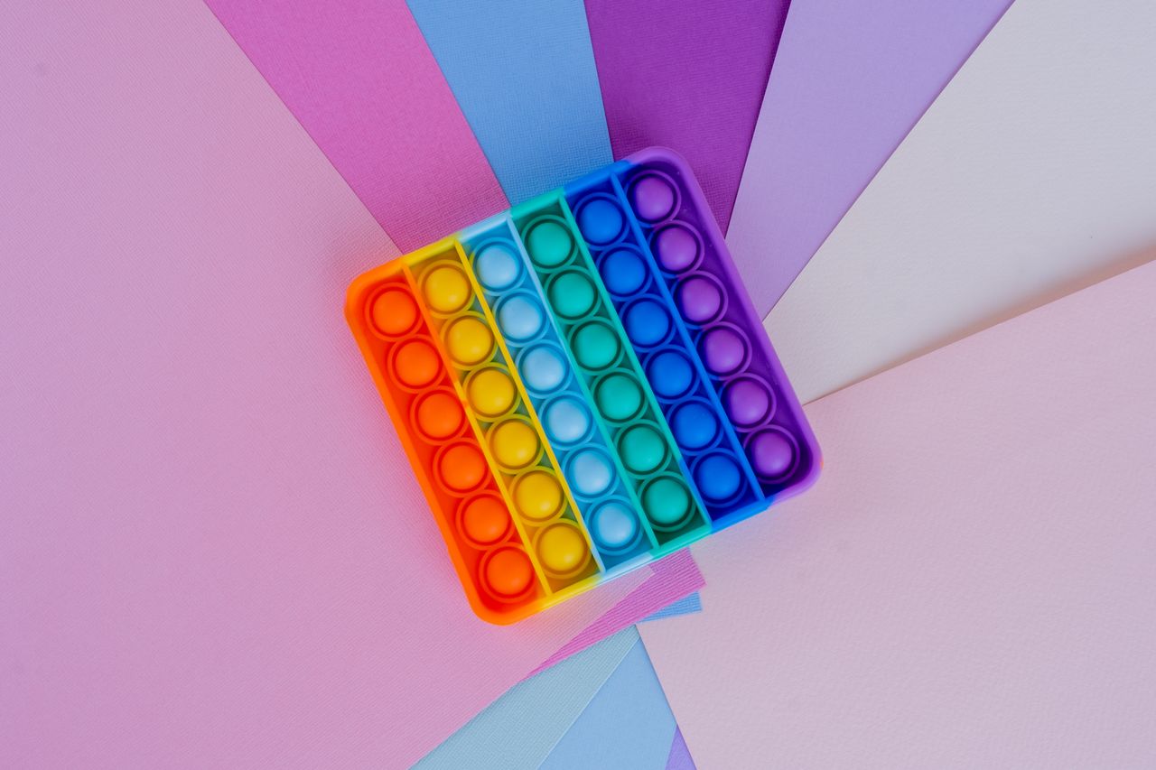 Rainbow pop it toy displayed on vibrant colored papers creating a playful scene.